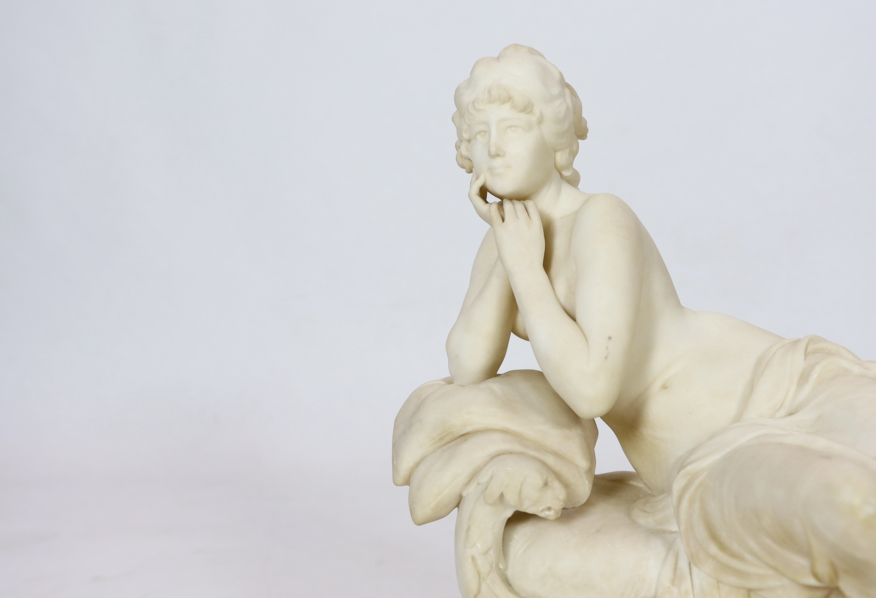 An early 20th century French carved white marble figure of a semi-clad woman seated upon a daybed, 50cm wide, 29cm deep, 52cm high